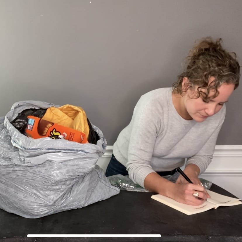 woman standing next to a trash bag and writing in a notebook