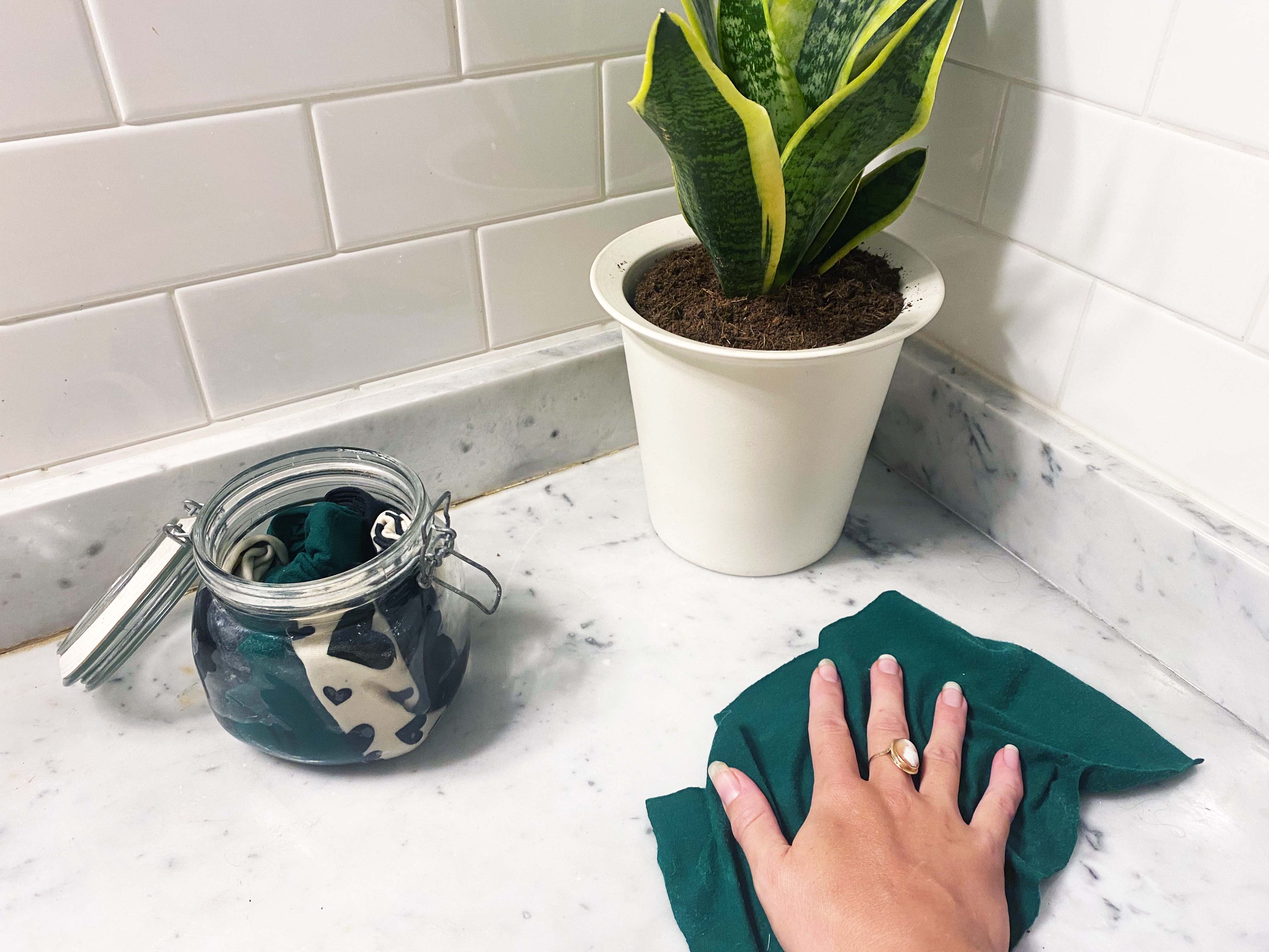 hand using fabric wipe next to jar of rolled up fabric and houseplant