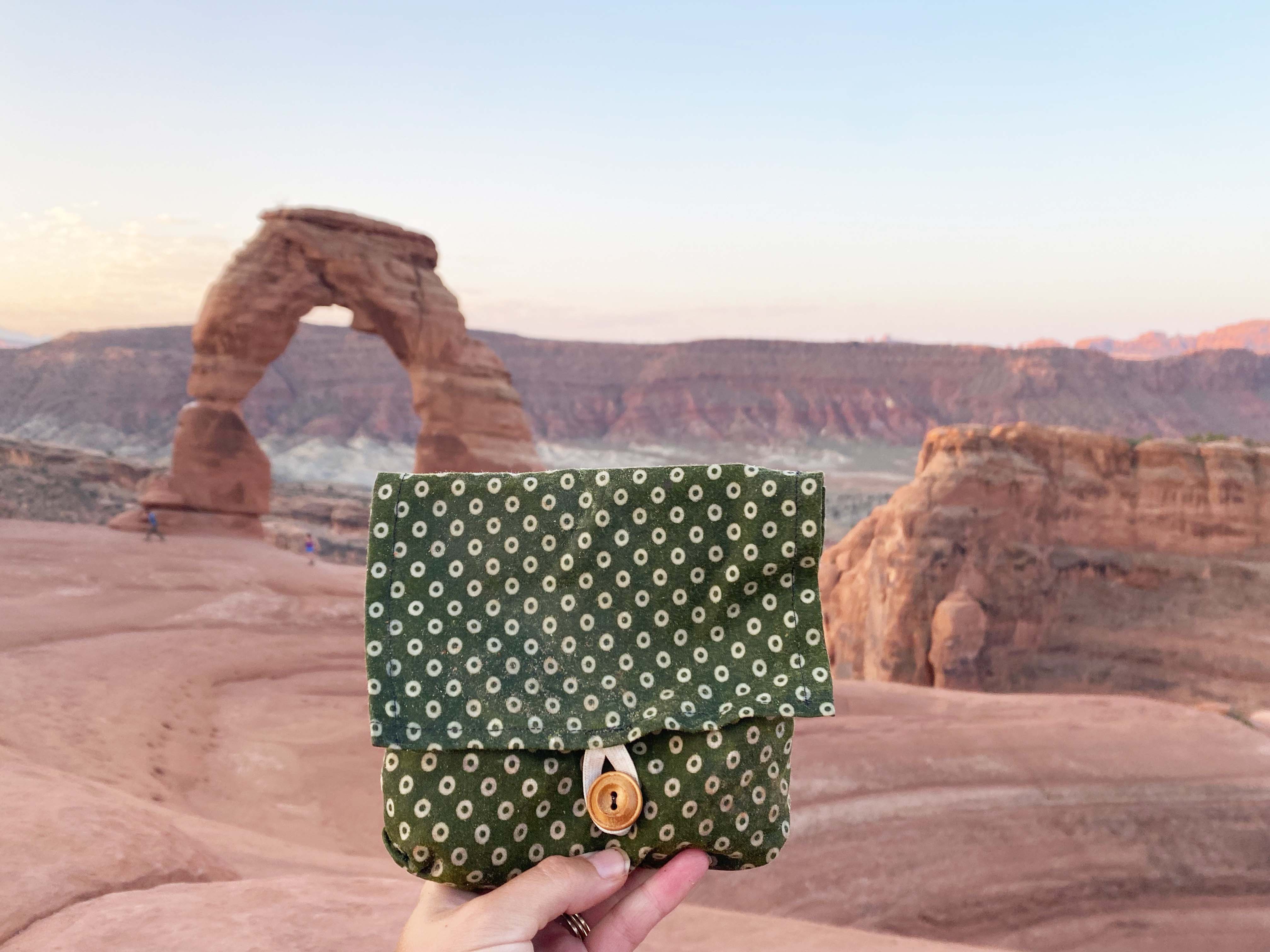 hand holding sandwich size cloth bag in front of Utah's Delicate Arch