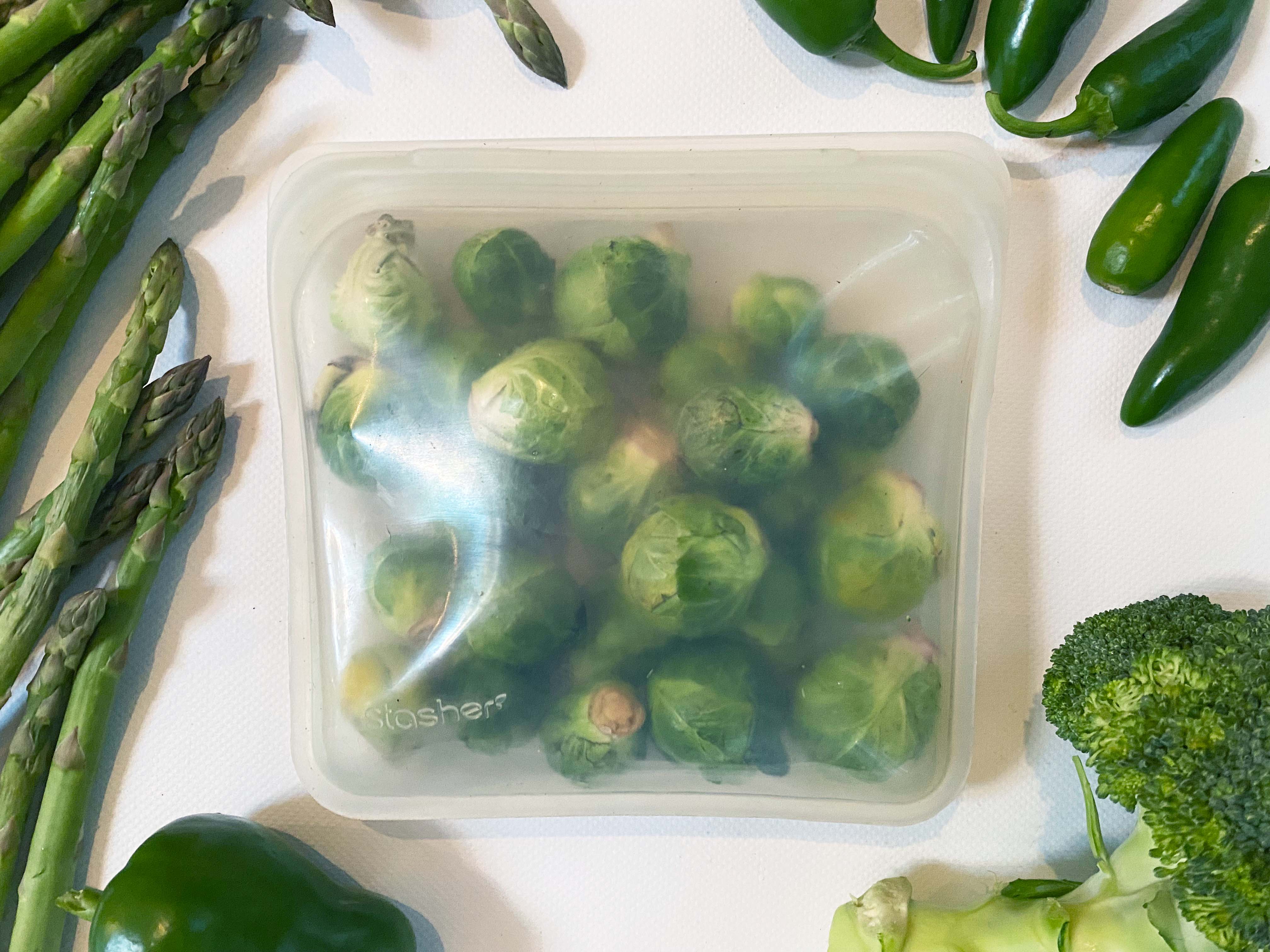 stasher silicone bag full of brussel sprouts surrounded by peppers, asparagus and broccoli