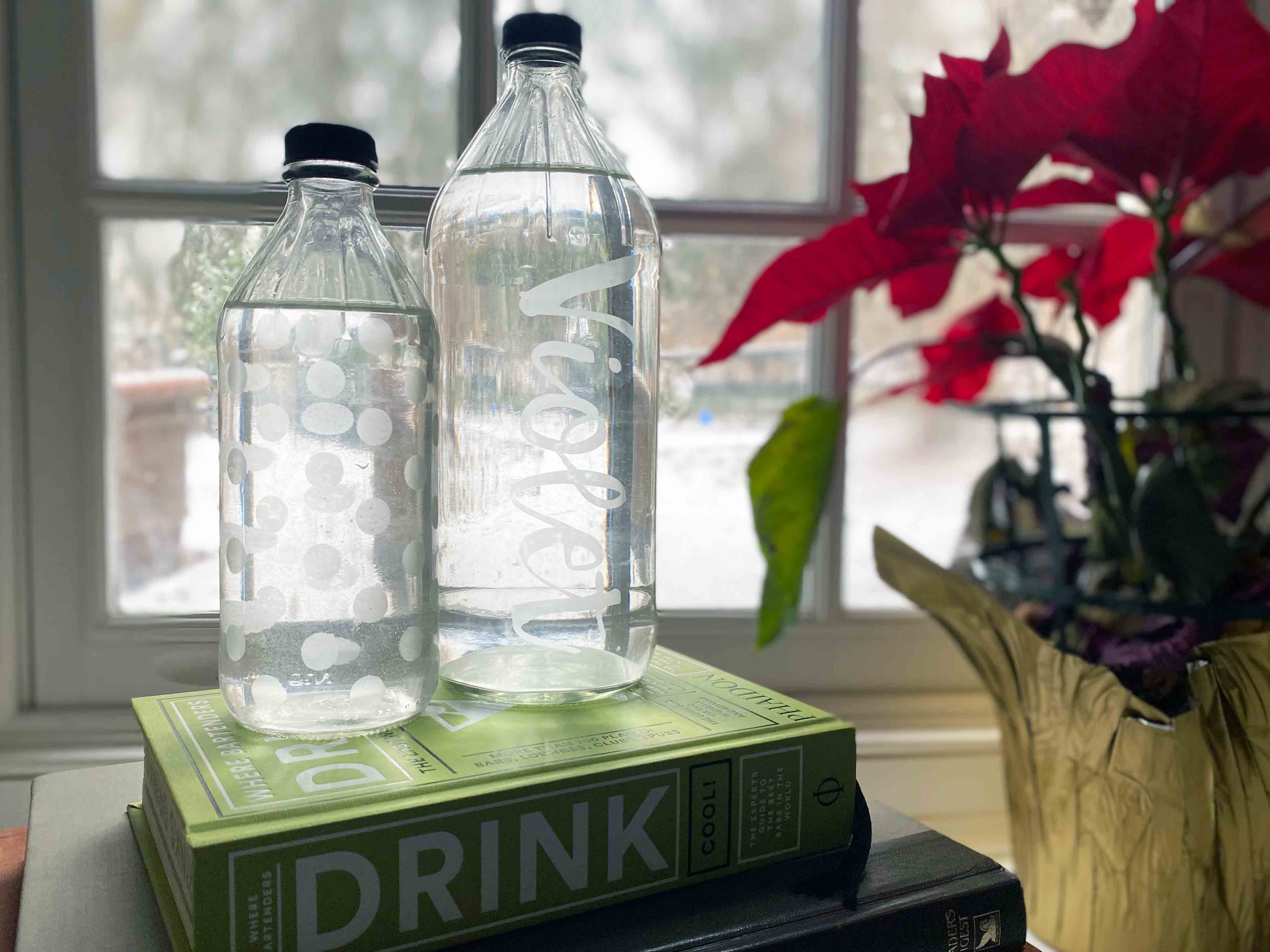 two etched glass bottles on a stack of books on a window sill